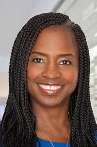A woman with braids is smiling and wearing a blue shirt.