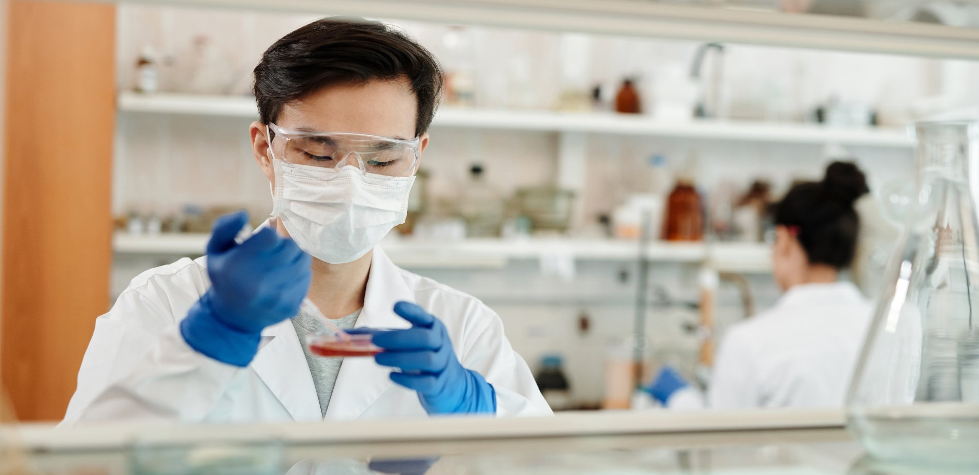 A scientist wearing a mask and gloves is working in a laboratory.
