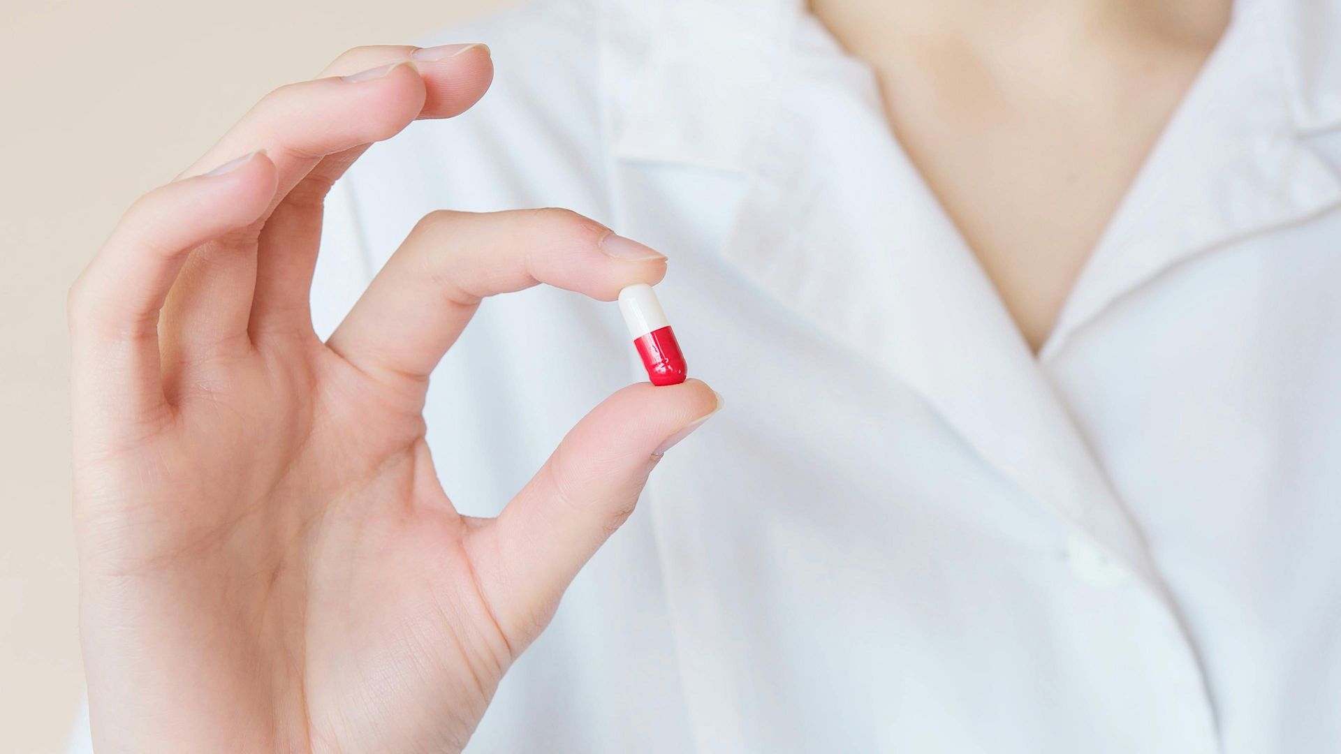A doctor is holding a red and white capsule in her hand.