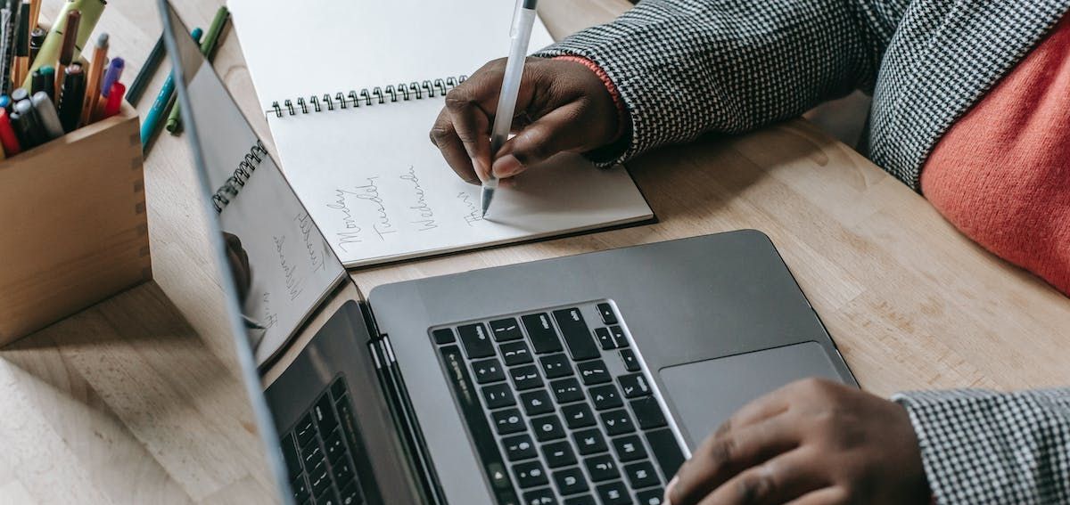 a person is writing in a notebook next to a laptop
