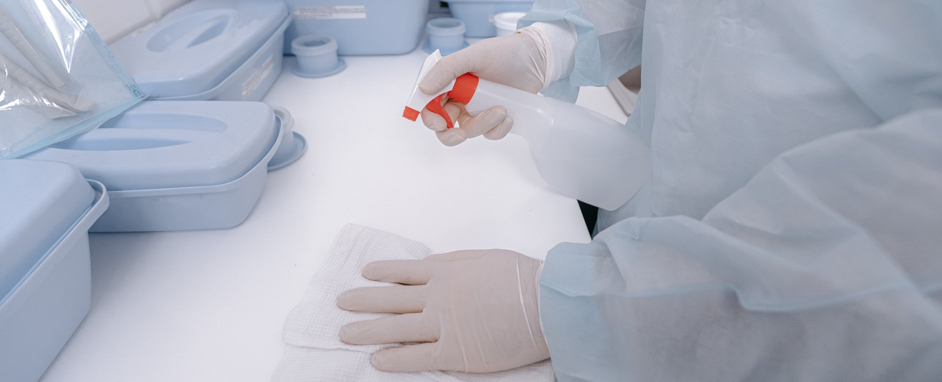 A person wearing gloves is cleaning a table with a spray bottle.