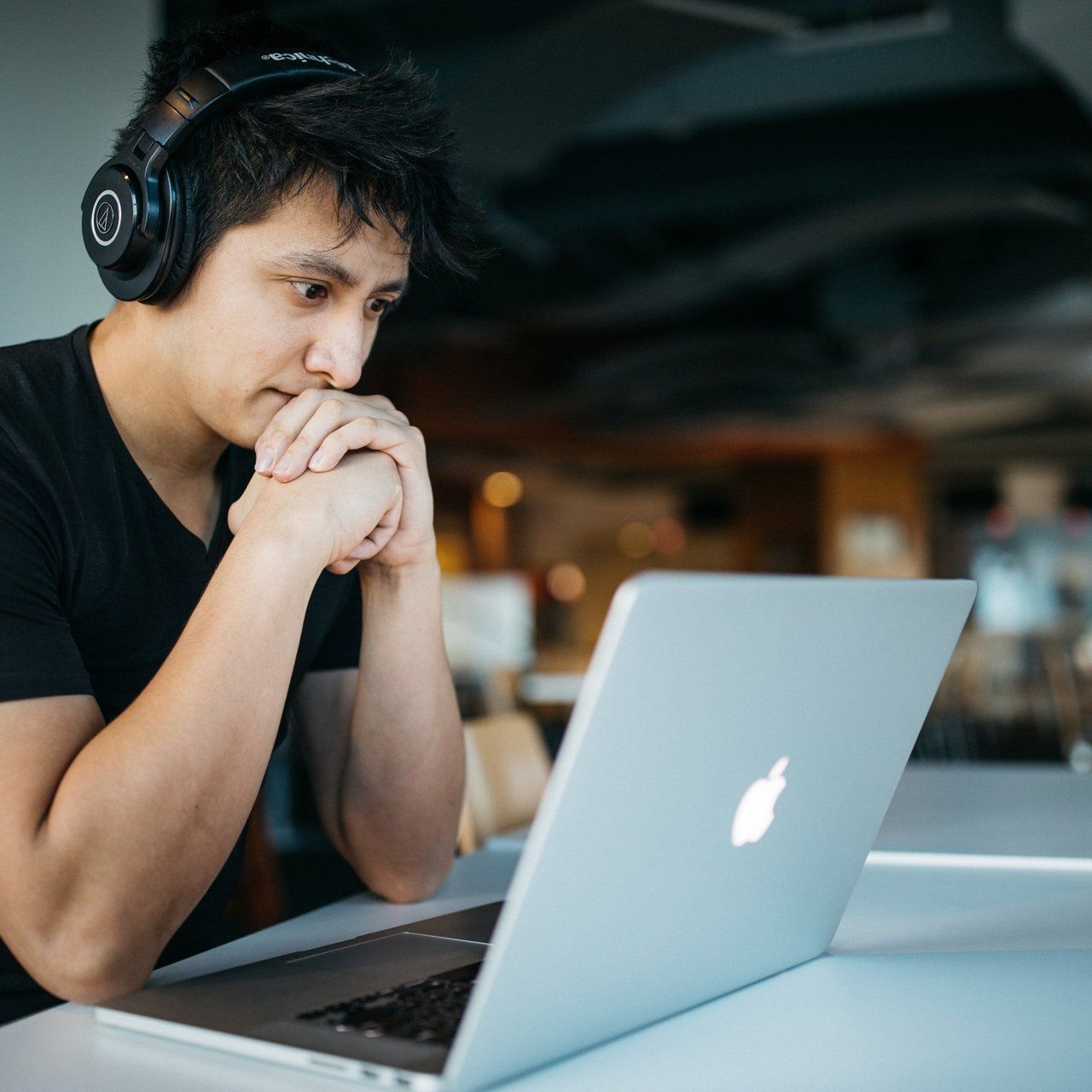 A man wearing headphones looks at an apple laptop