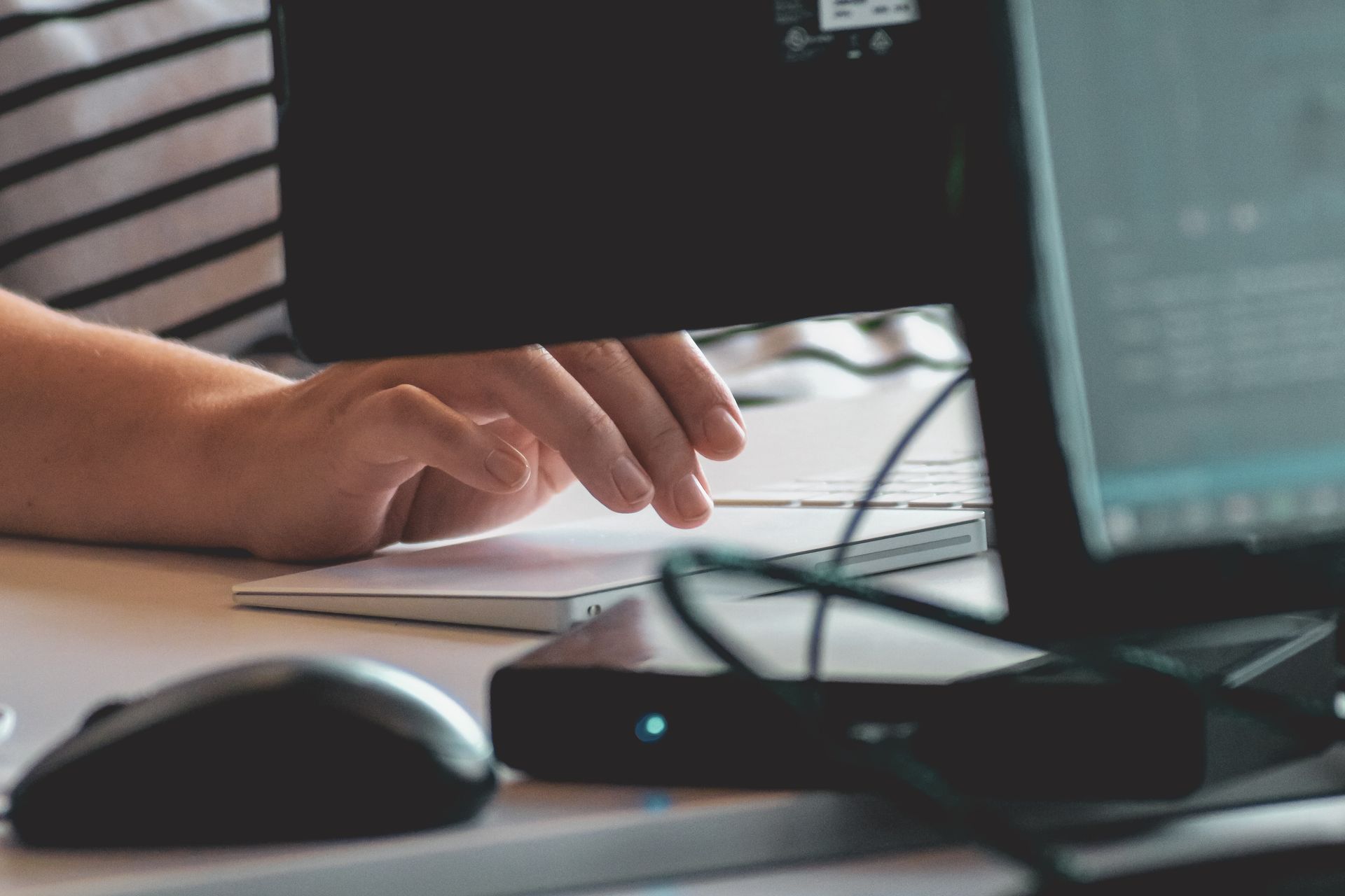 A person is typing on a laptop next to a mouse.