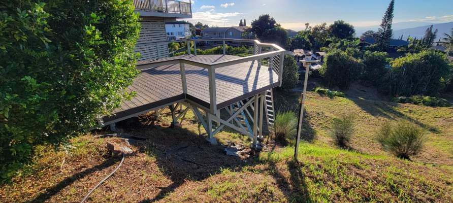 Wooden lookout deck on a grassy hillside, with trees and city buildings in the background.
