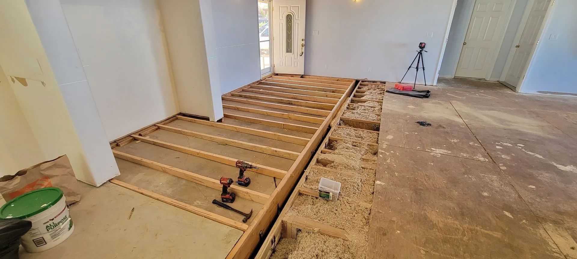 Unfinished room with exposed floor framing, tools, and plywood underlayment being installed