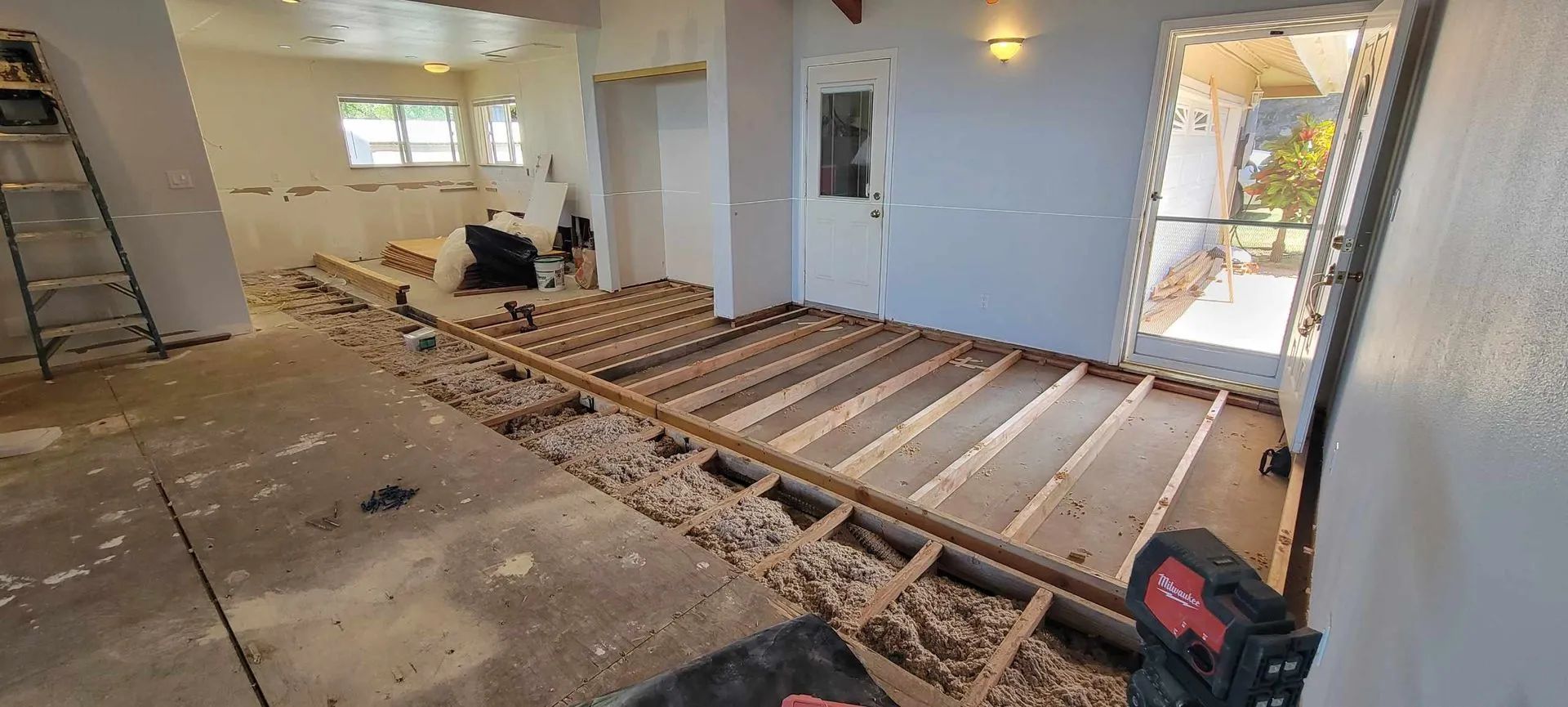 Interior room under renovation with exposed floor joists, tools, and a ladder near a doorway
