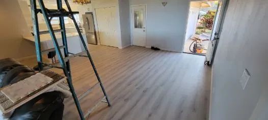 Empty room with a ladder, wood flooring, and an open door to the outside.
