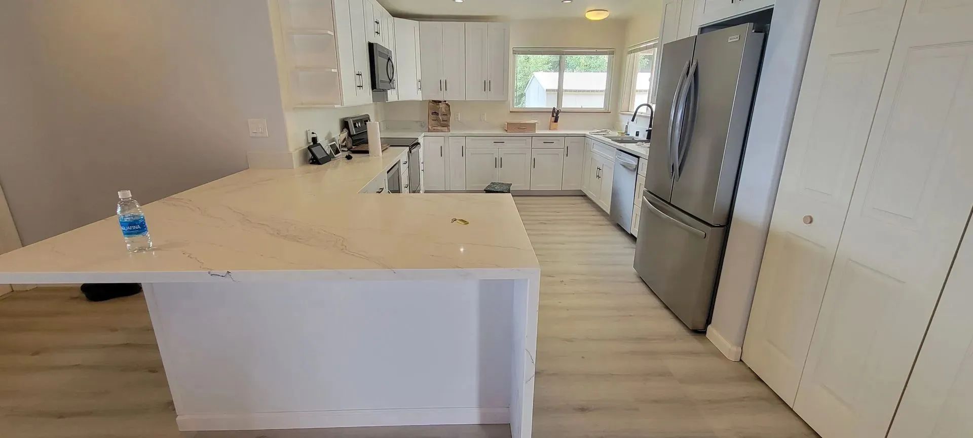 Bright modern kitchen with white island, stainless fridge, and sunlit window
