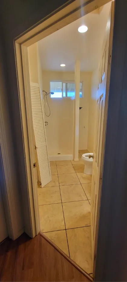 Narrow mirrored hallway leading to a tiled bathroom with a toilet and shower visible.