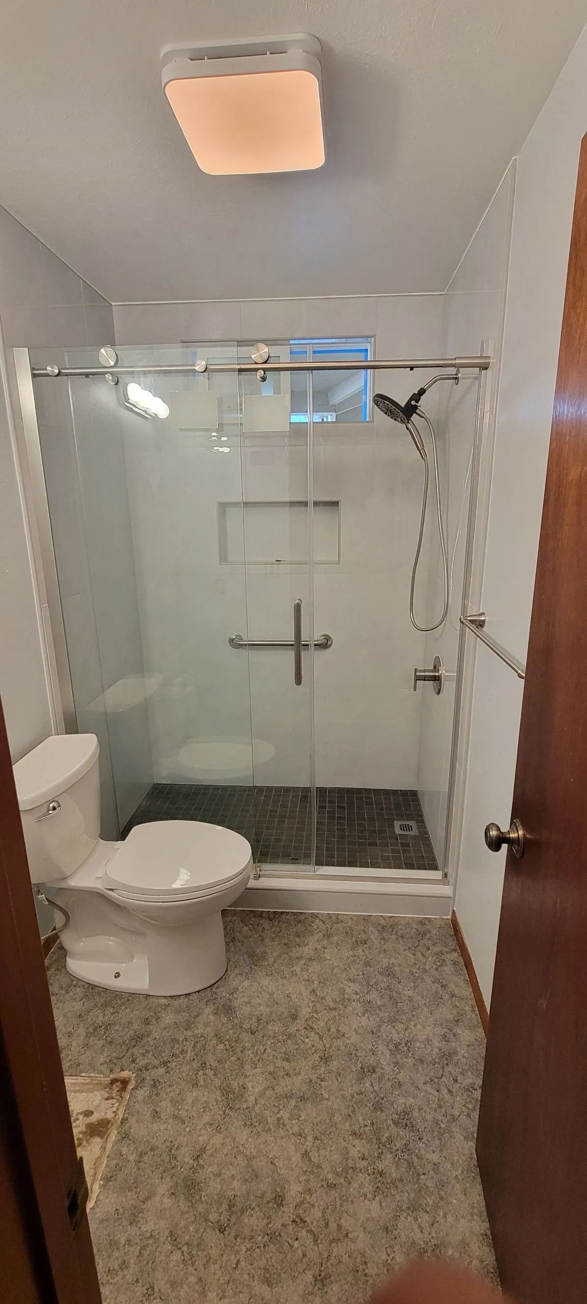 Small bathroom with glass walk-in shower, toilet, and beige tile floor.