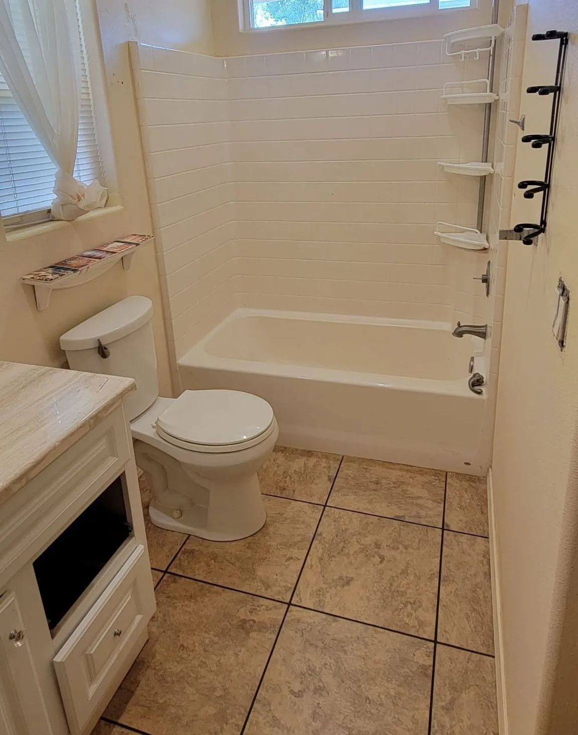 Small bathroom with white tub, toilet, sink vanity, and beige tile floor.