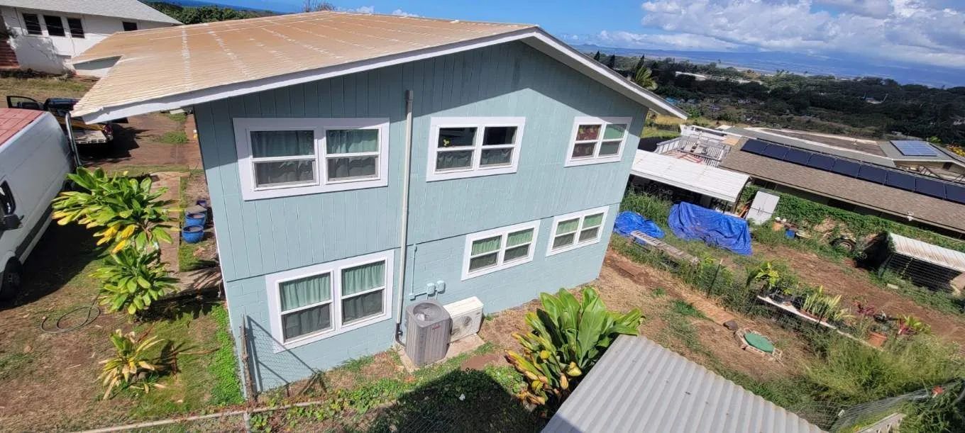 Light blue two-story house with white-trimmed windows on a hillside overlooking greenery and rail tracks