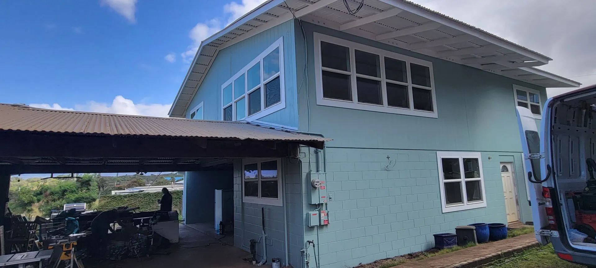 Blue two-story house with a carport, white-trim windows, and a sloped roof under a clear sky