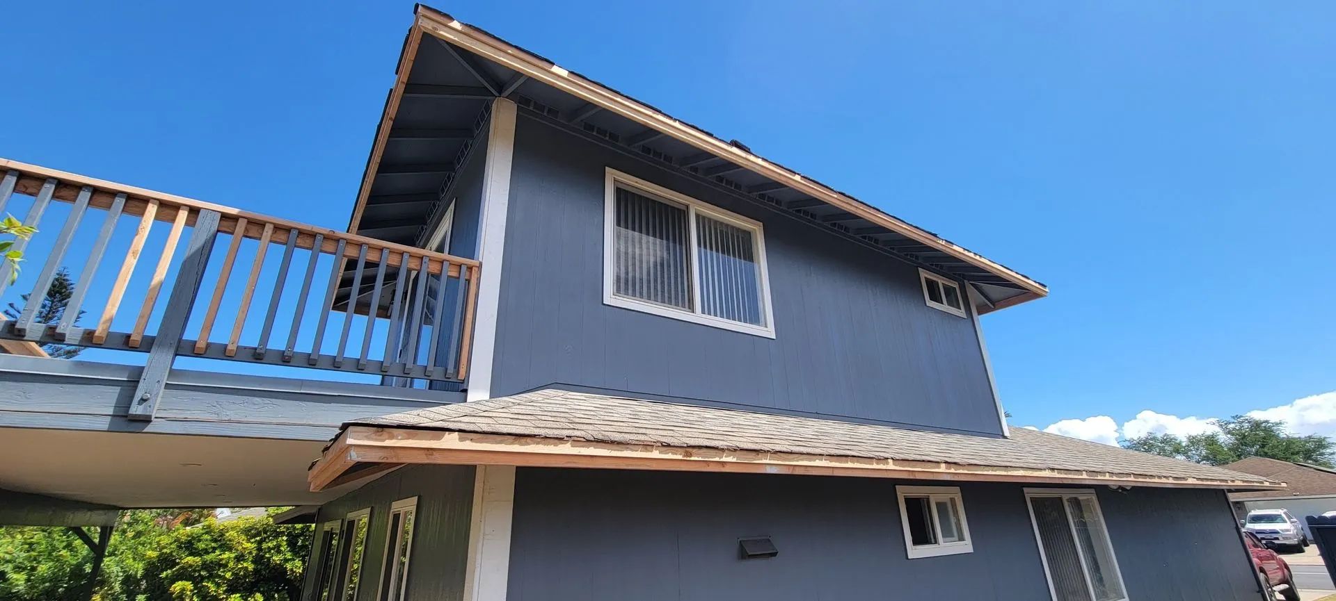 Blue two-story house with white trim and a balcony, viewed from below in daylight