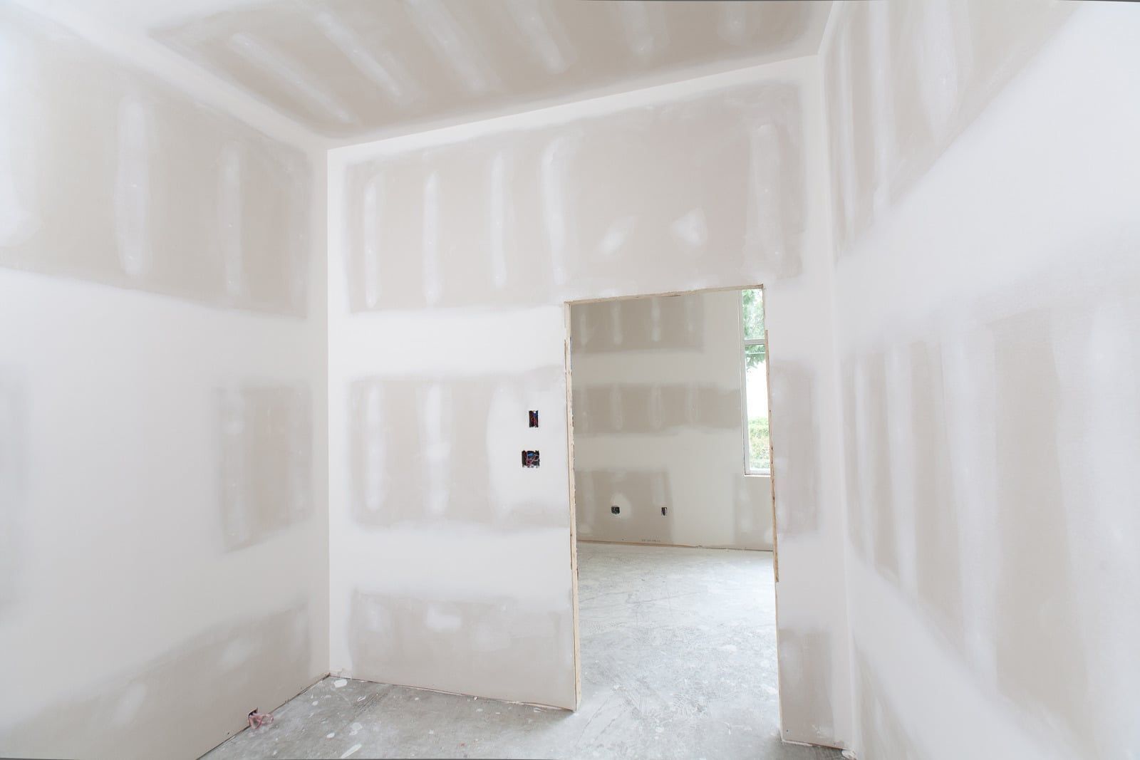 Unfinished drywall room with taped seams, doorway, and light coming from a larger room beyond.