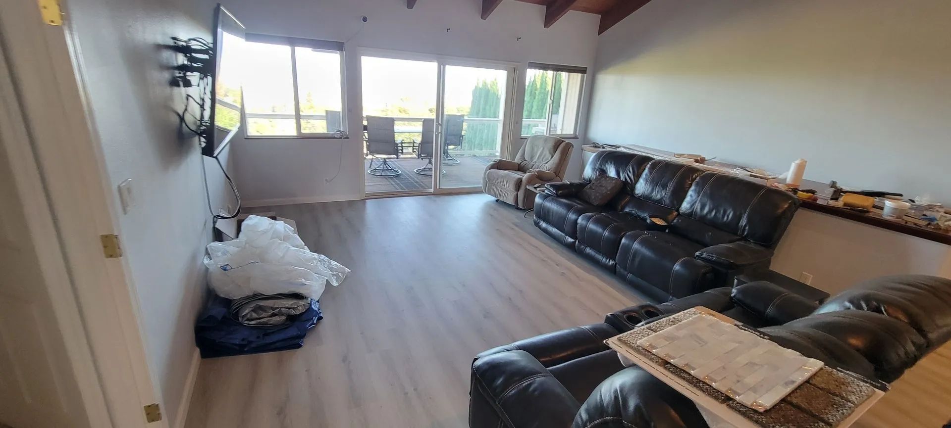 Bright living room with black leather sofas, wood floors, and large windows.