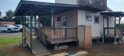 Covered wooden porch ramp attached to a small beige house on a wet day