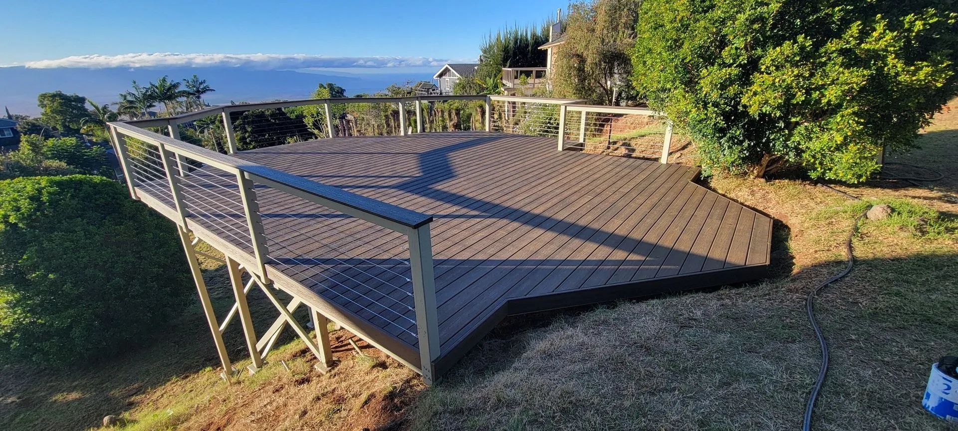 Wooden deck overlooking the ocean, with railing, greenery, and a sunny coastal view