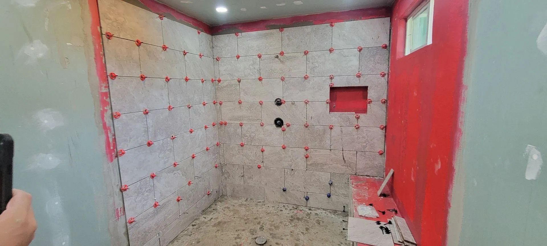 Renovation site with white tiled wall, red paint, and unfinished floor in a small room