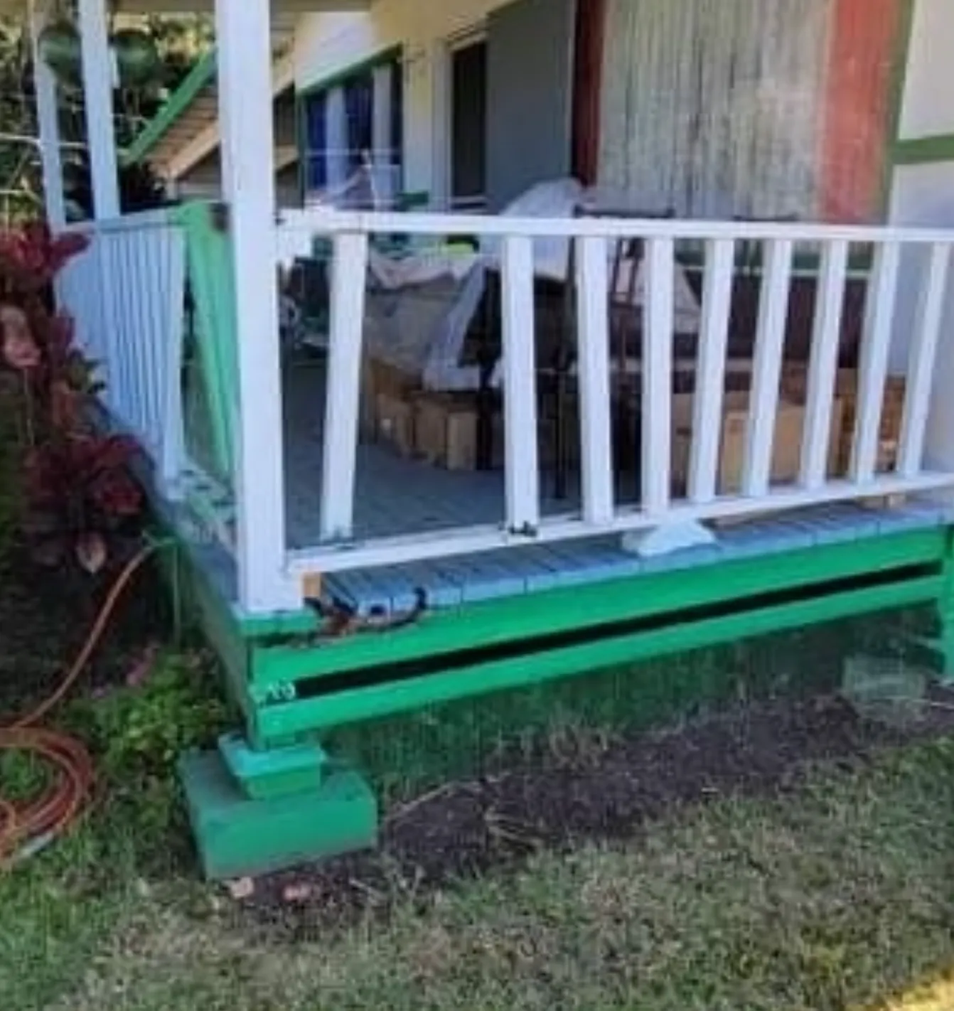 Green-painted porch with white railing and steps, with a small garden area beside it.