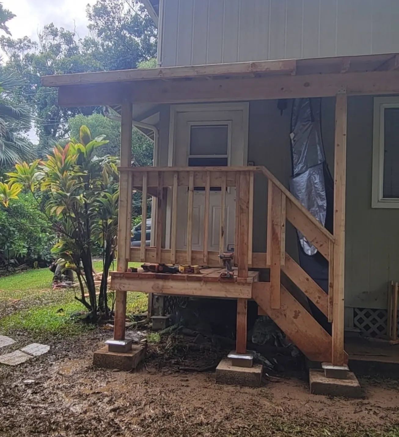 Small wooden porch and stairs on a house, with concrete supports and a tarp-covered side wall.