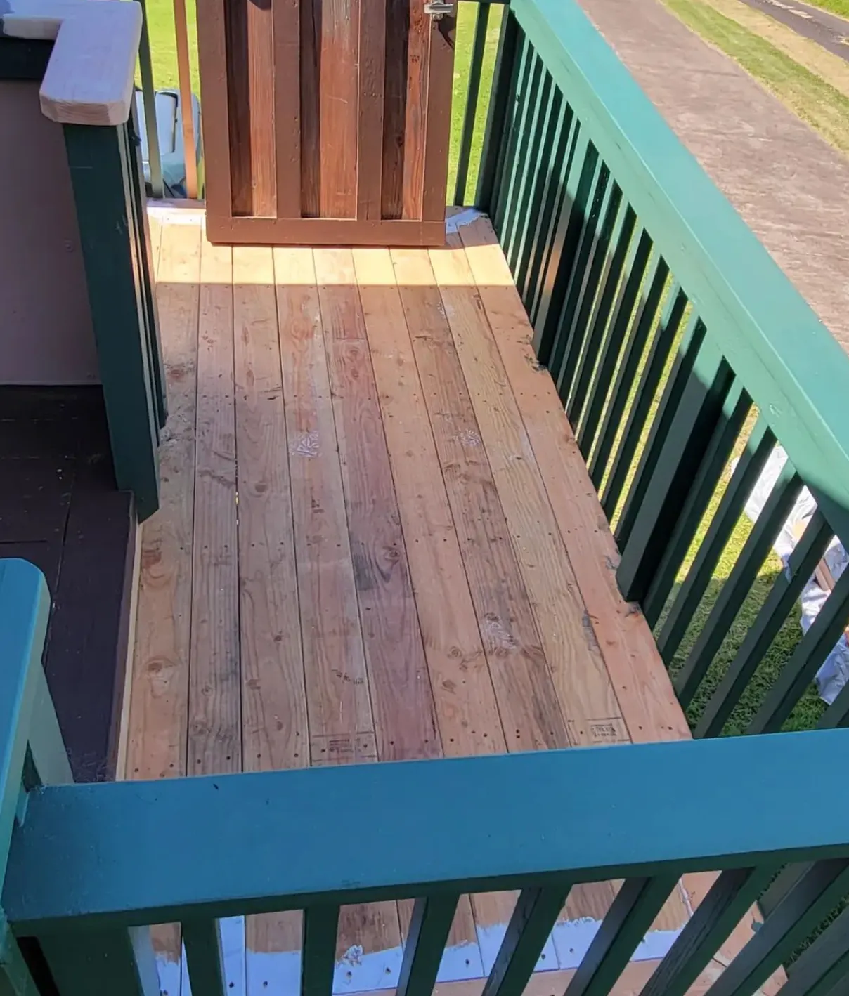 Wooden balcony deck with green railings and a small gate, overlooking a road.