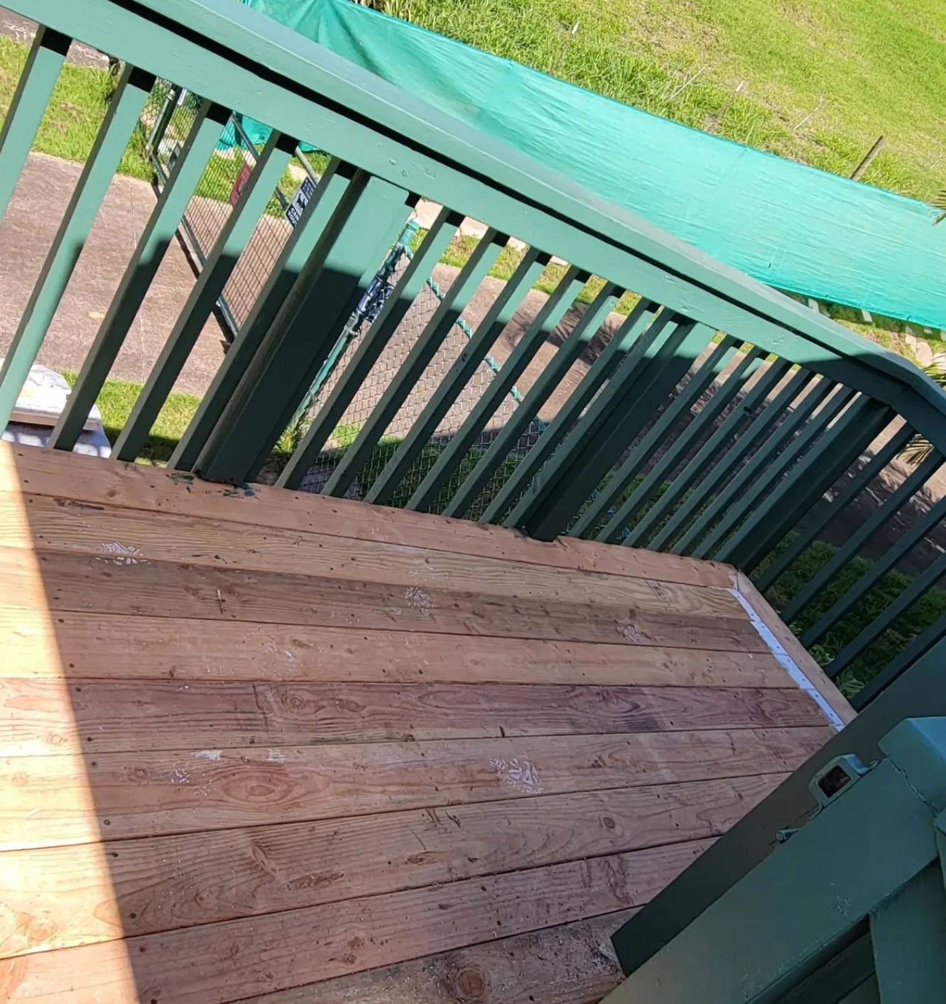 Wooden deck with green railing and grass beyond, viewed from a corner.