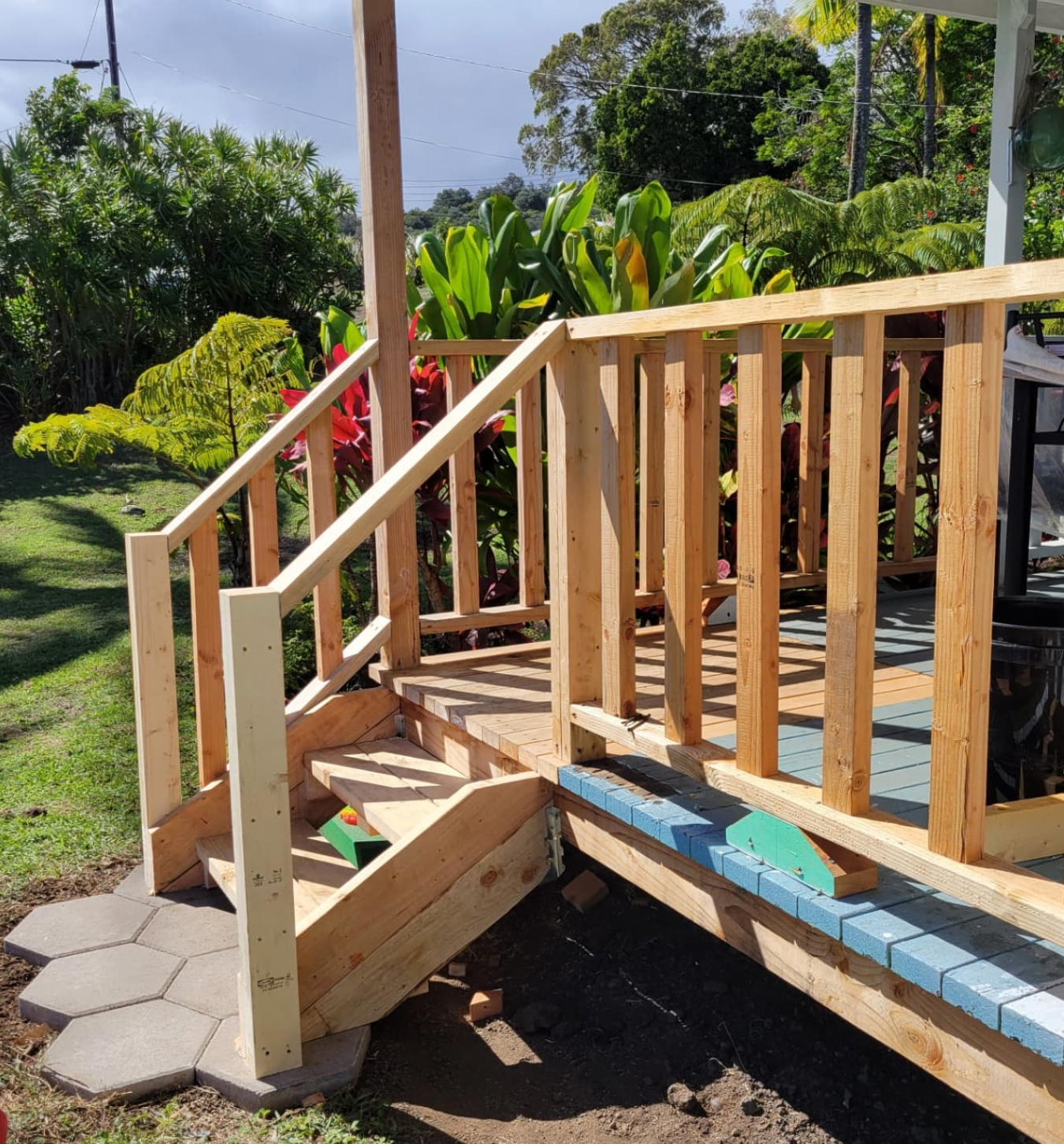 Wooden porch stairs with railing beside a sunny garden and stone path