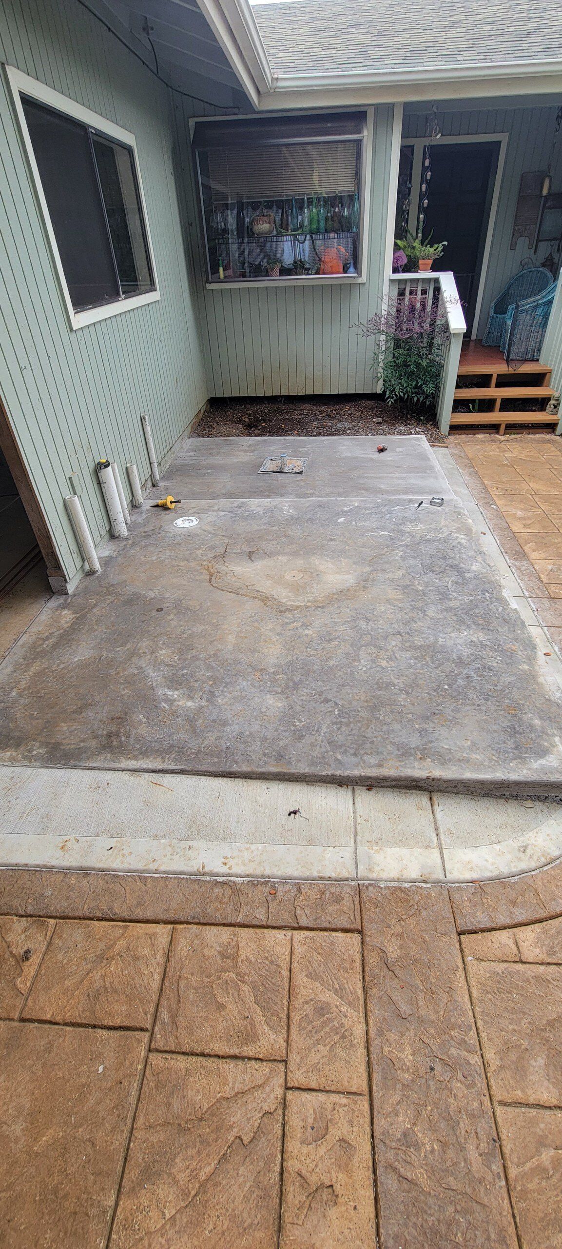 Empty concrete patio area beside a house, with a window, doorway, and tiled floor edge.