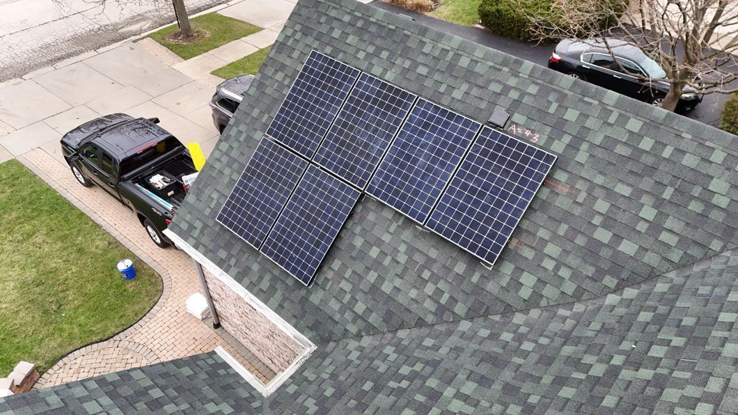 Solar panels installed on a green shingled roof; a black truck and car are visible in the setting.