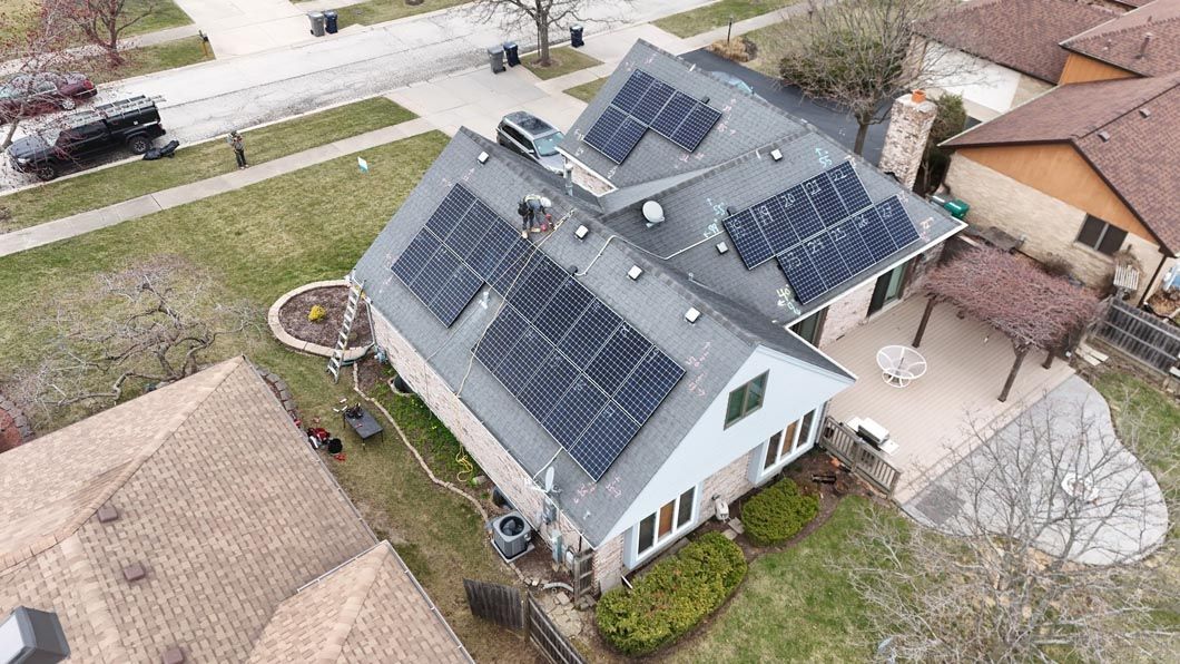 Overhead view of a house with solar panels on the roof, surrounded by green grass, and other houses in the neighborhood.