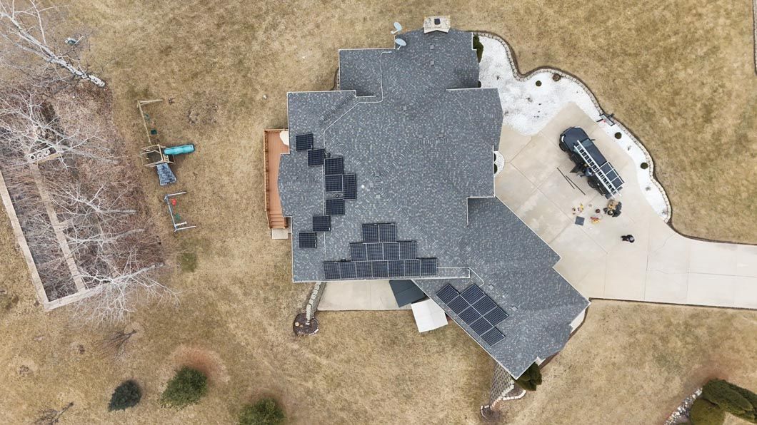 Aerial view of a house with solar panels on the roof, surrounded by brown grass and a driveway.