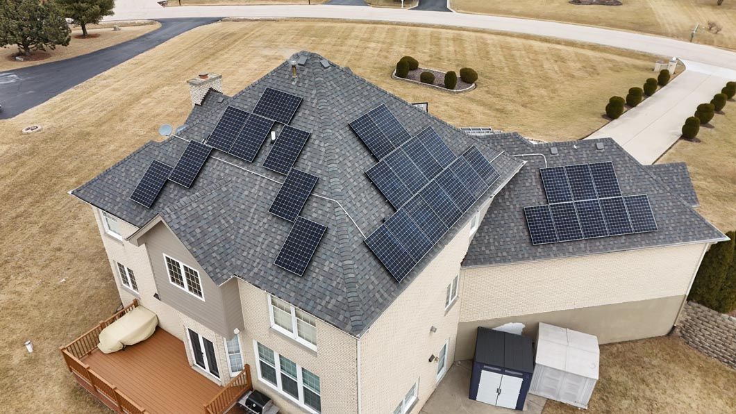 Solar panels on a two-story house with a brown lawn and driveway.