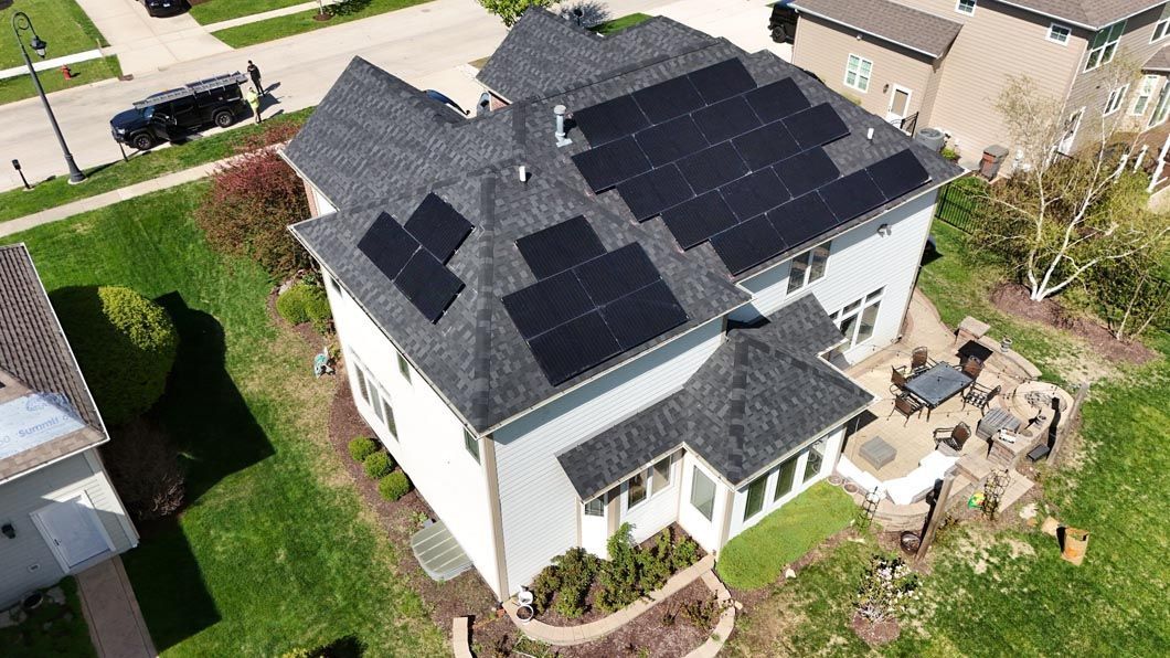 House with solar panels on the roof, surrounded by green grass, a driveway, and other houses.