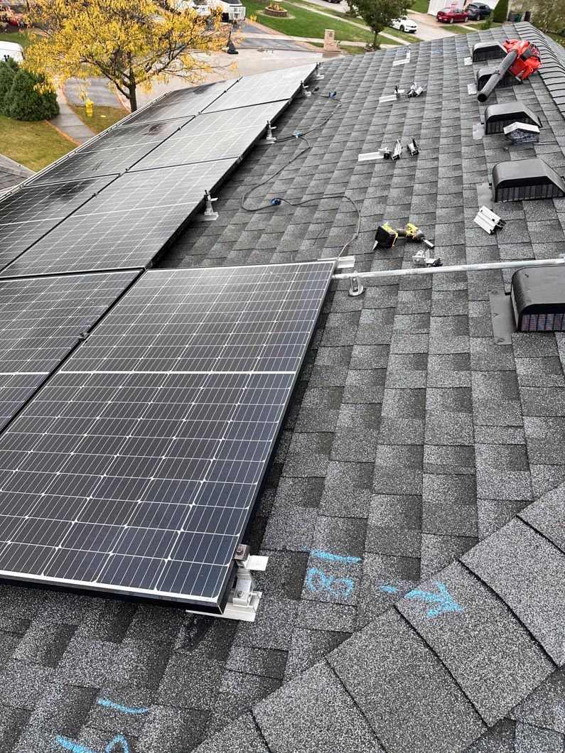 Solar panels being installed on a gray shingle roof. Tools and equipment are scattered nearby.