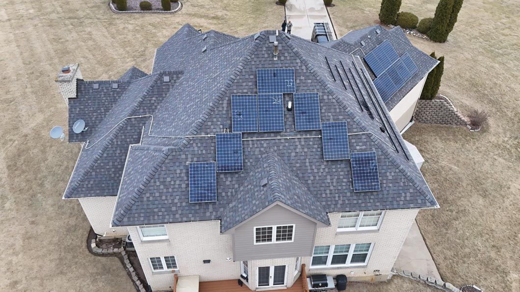 Overhead view of a house with solar panels on the roof, on a grassy lot, neutral color.