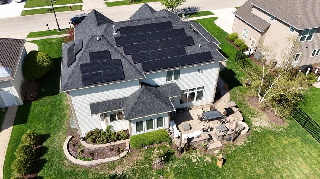 Aerial view of a house with solar panels on the roof, surrounded by green grass, in a suburban neighborhood.