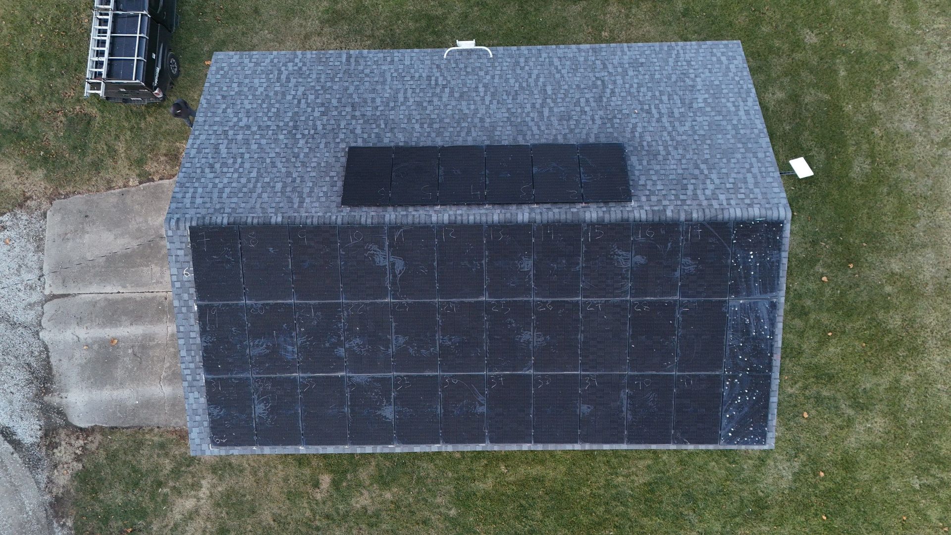 Overhead view of a house with solar panels on the roof and steps leading to the entrance. Green lawn surrounds.