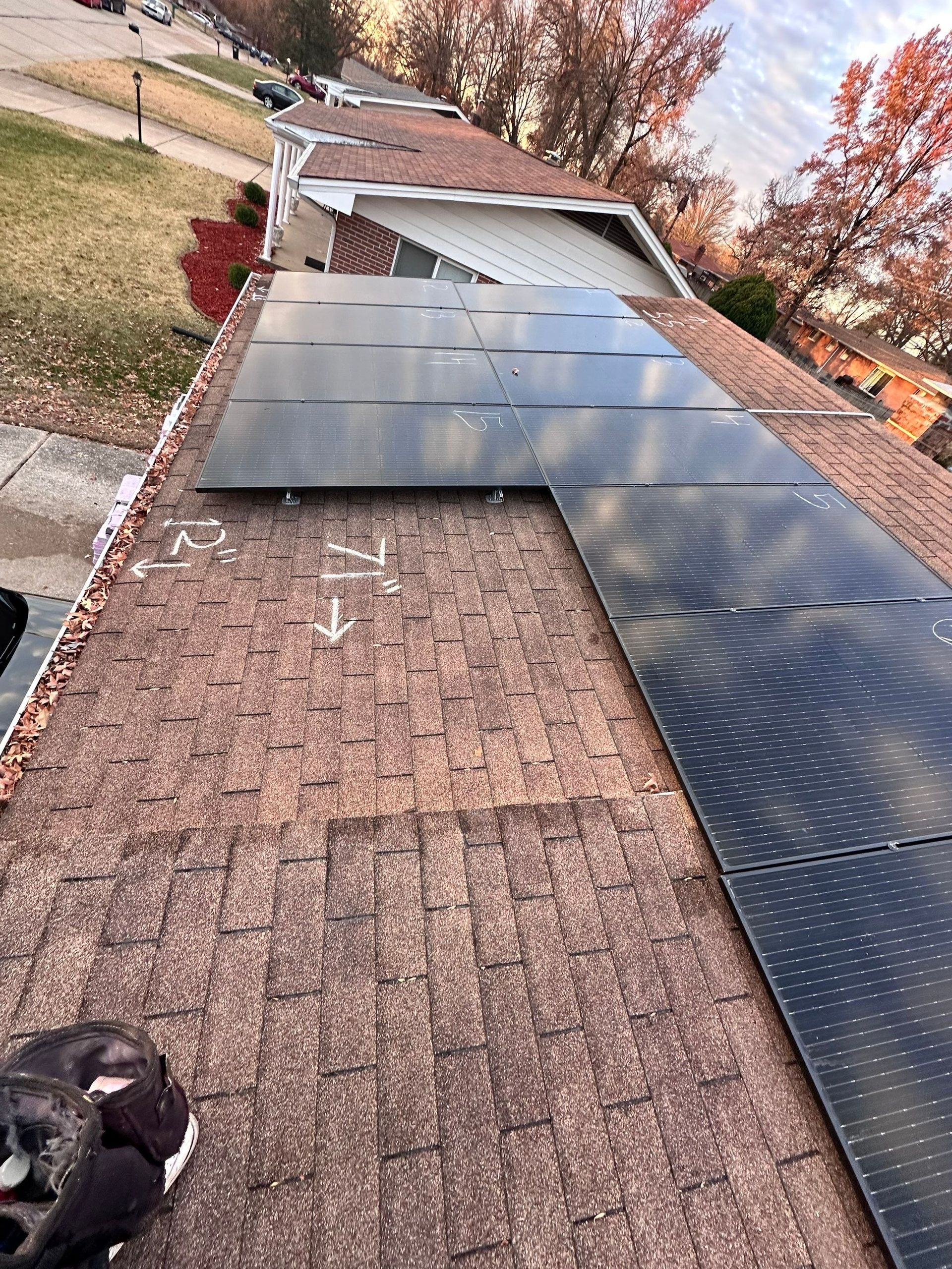Solar panels being installed on a brown shingled roof in a residential neighborhood.