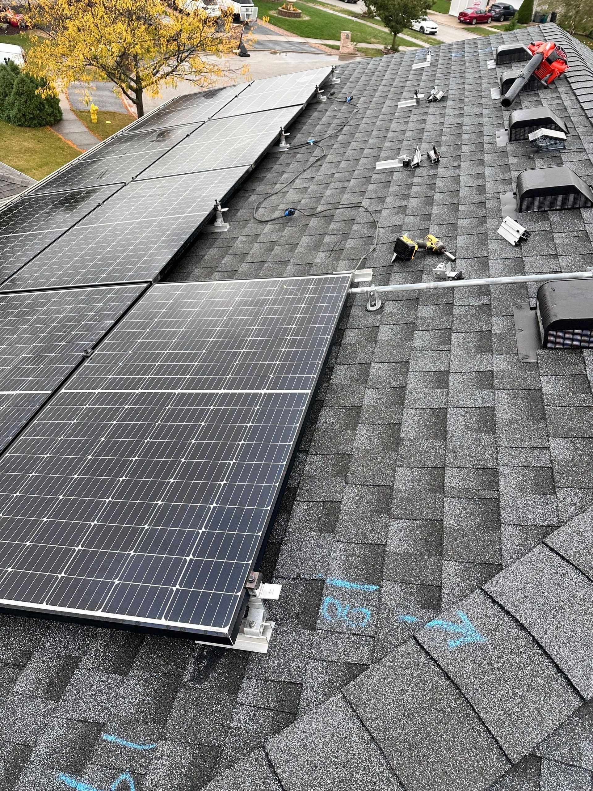 Solar panels installed on a dark shingle roof. Construction tools visible.