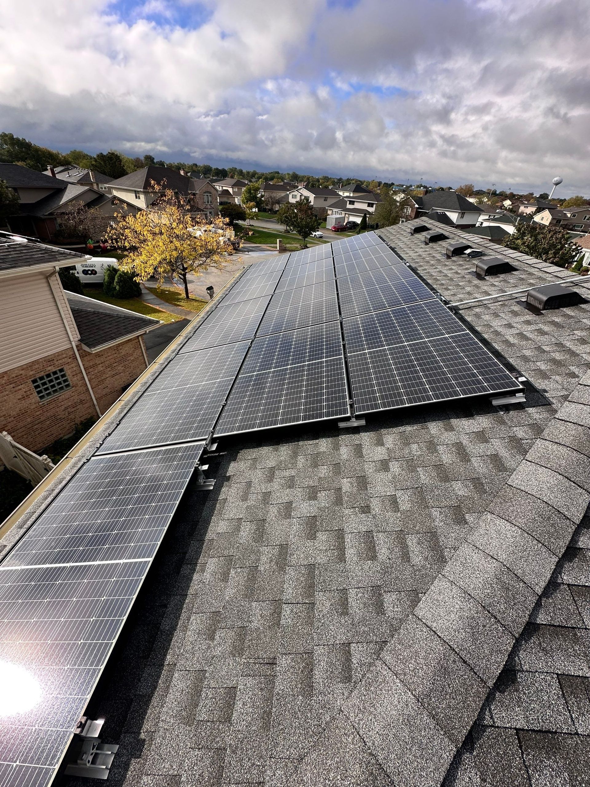 Solar panels on a residential roof, capturing sunlight against a cloudy sky and suburban backdrop.