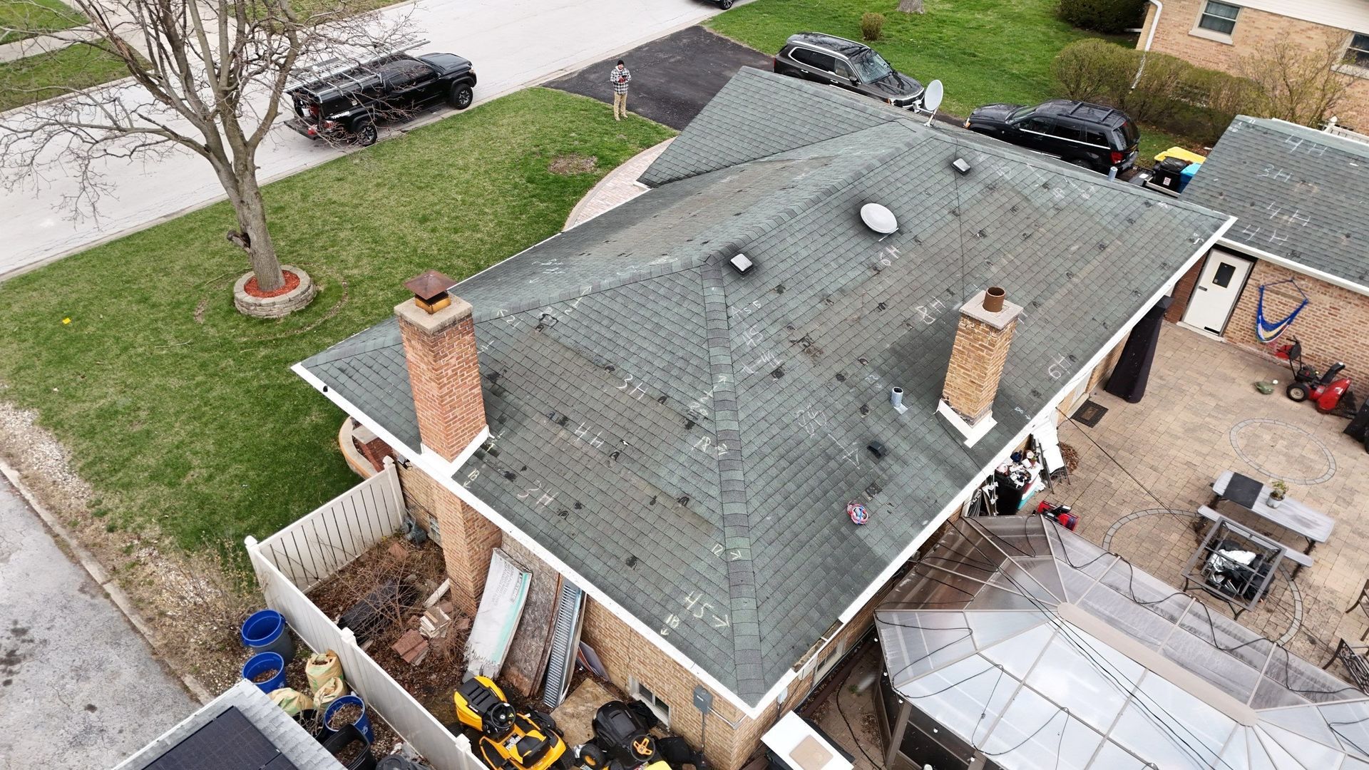 Overhead view of a brick house with a gray roof, two chimneys, and a white fence.