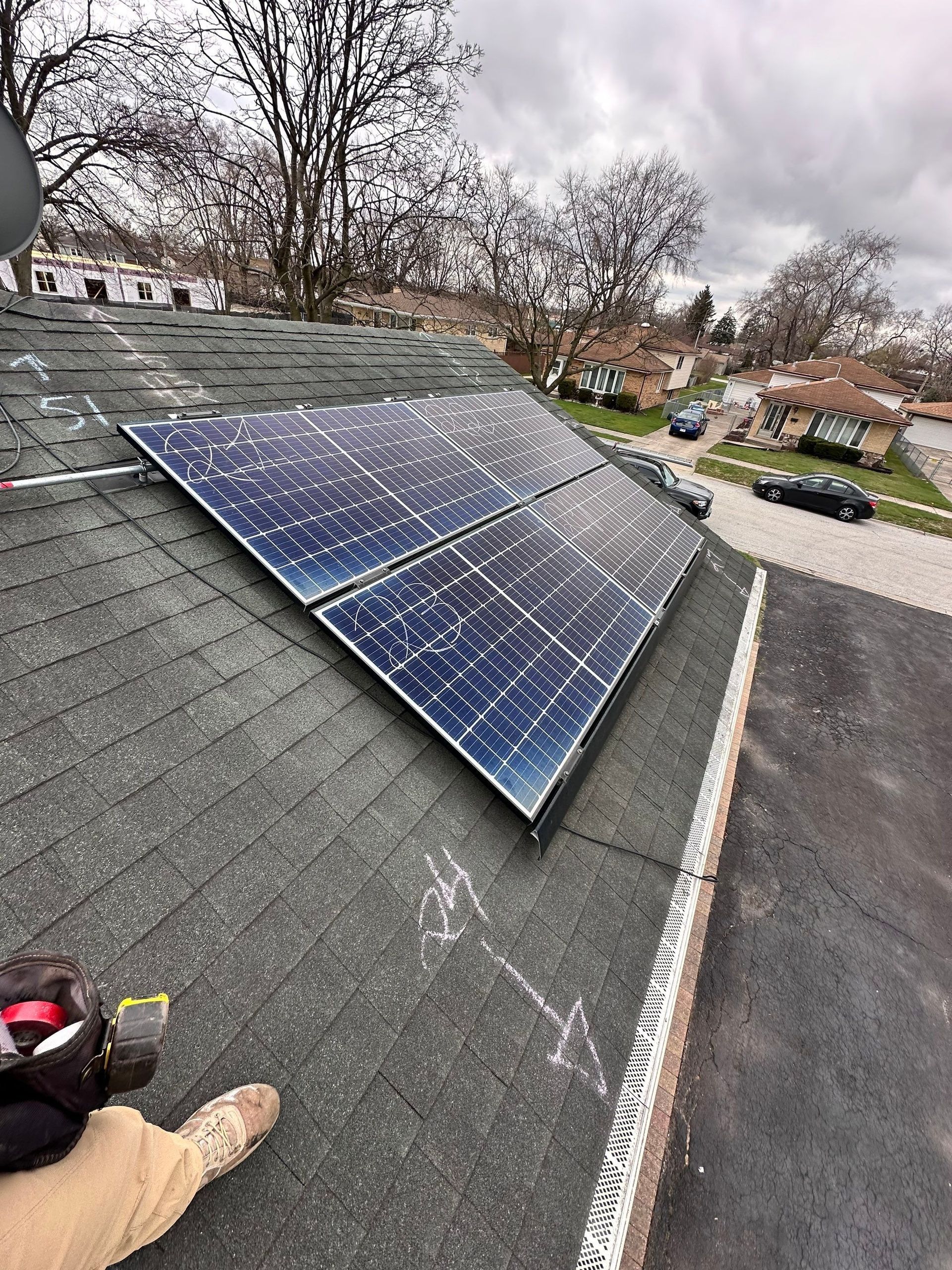 Solar panels installed on a dark shingle roof; a person in work clothes sits nearby.
