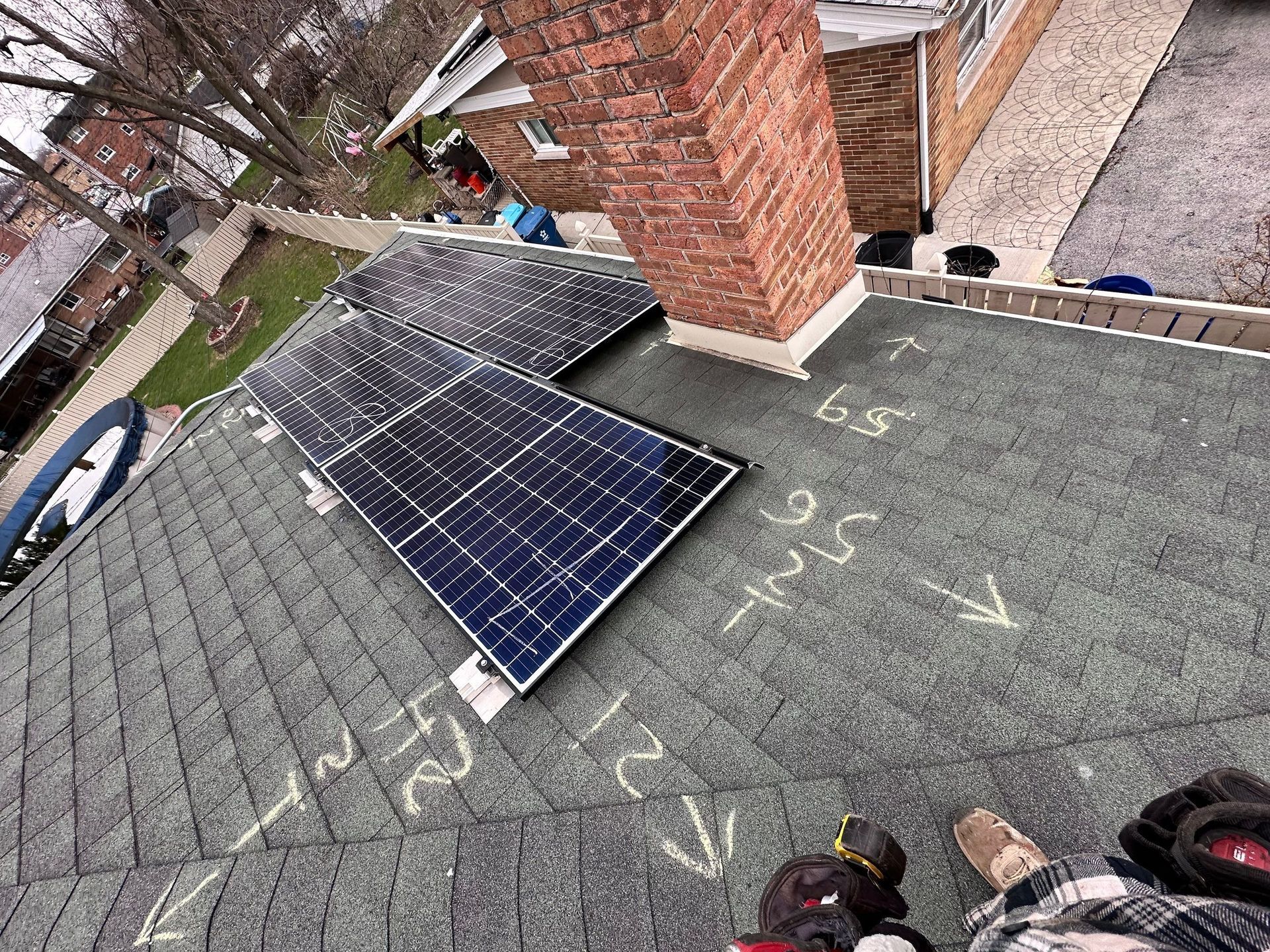 Solar panels installed on a gray shingled roof near a brick chimney. Arrows and measurements are marked on the roof.