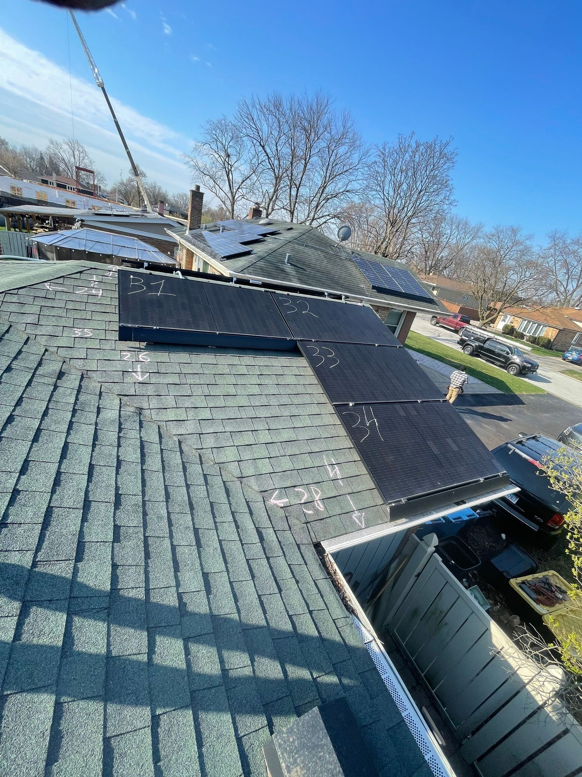 Solar panels on a gray shingled roof, sunny day. Gutters in the foreground. Trees in the background.