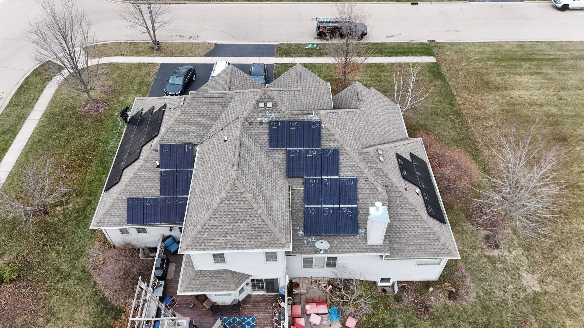 Aerial view of a house with solar panels installed on multiple roof sections, surrounded by a yard and a street.