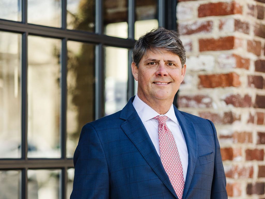 Harlan F. Winn, III wearing a suit and tie standing in front of a brick building.