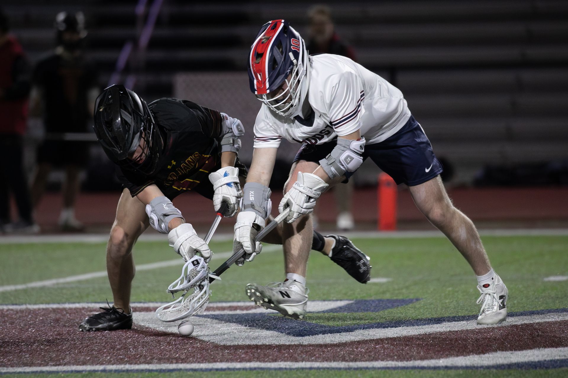 Two lacrosse players crouch at the faceoff on a lit field at night.