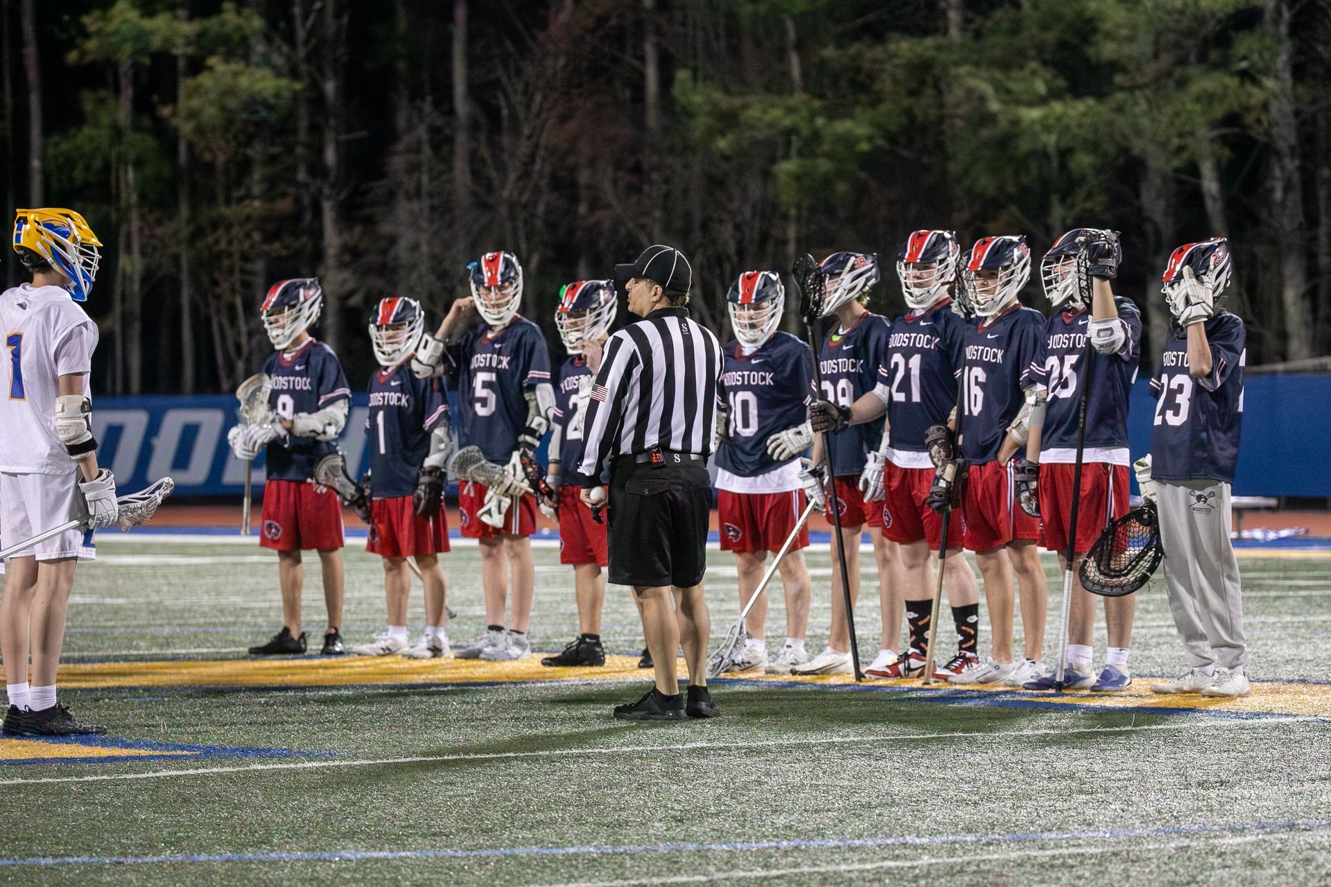 Lacrosse teams lined up at midfield for the opening faceoff under stadium lights.