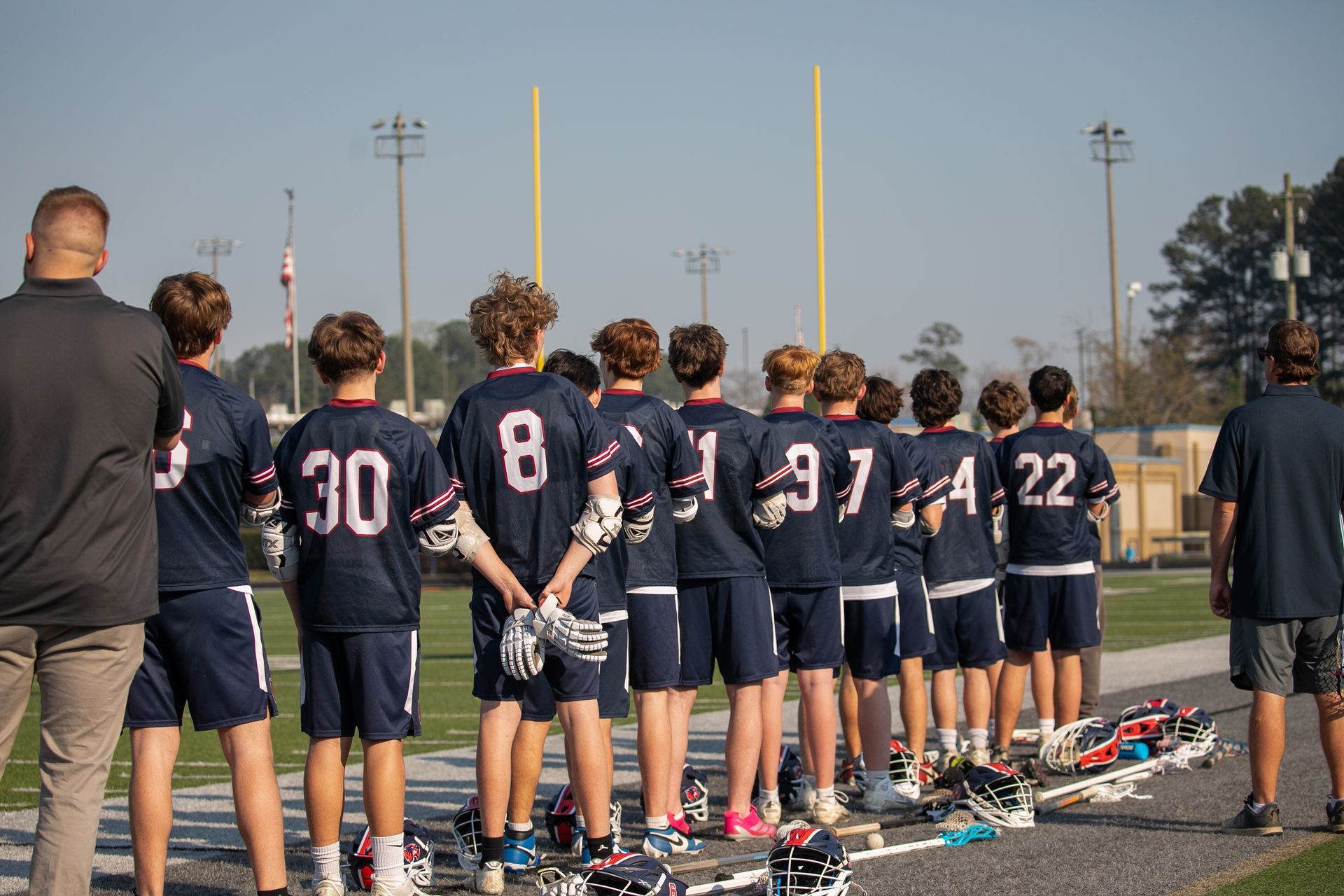 Youth baseball team lined up on a field, facing away during a pregame ceremony.